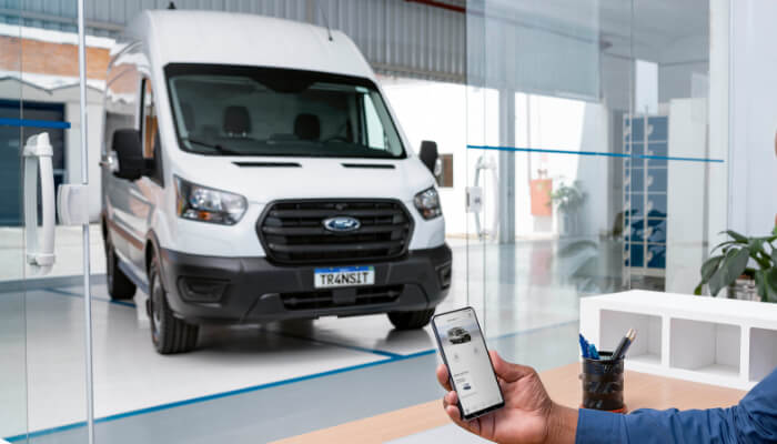 Ford Transit Furgão ao fundo e homem com celular e aplicativo FordPass na tela