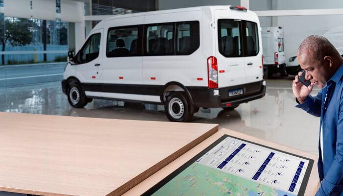 Ford Transit Minibus ao fundo e homem falando ao celular e consultando tela com mapa