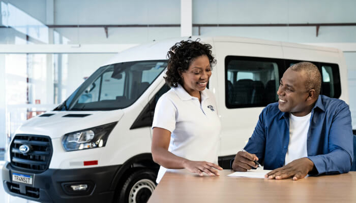 Ford Transit Minibus ao fundo, com homem e mulher verificando documento