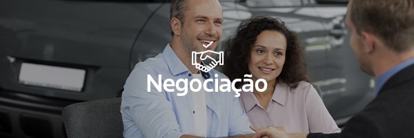 Dois homens apertando as mãos, uma mulher ao lado e um veículo Ford ao fundo