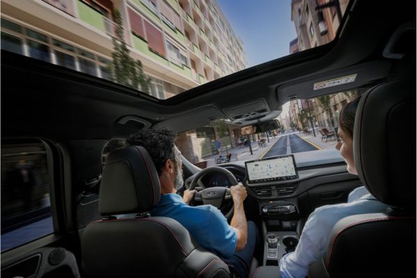 Due persone siedono a bordo di un veicolo Ford e attraversano la città