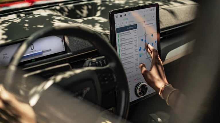 Écran navigation connectée Gros plan d’une femme assise dans une Ford Mustang Mach-E, interagissant avec le grand écran tactile SYNC