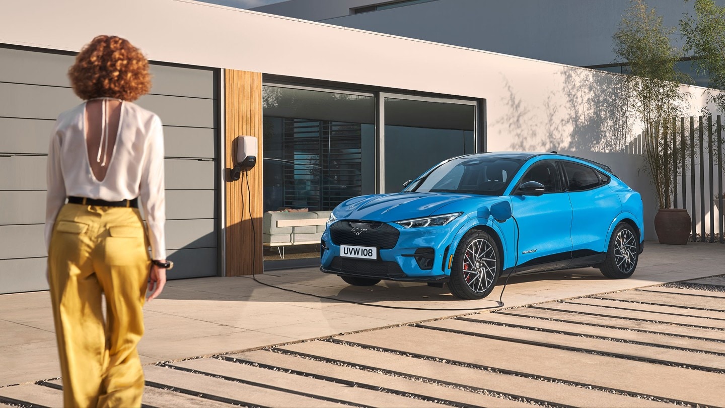 Ford Mach-E bleue en charge avec femme qui marche devant